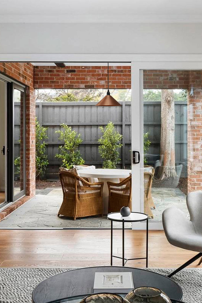 Copper cone shade with IP rated pendant cord over an outdoor, undercover dining space.