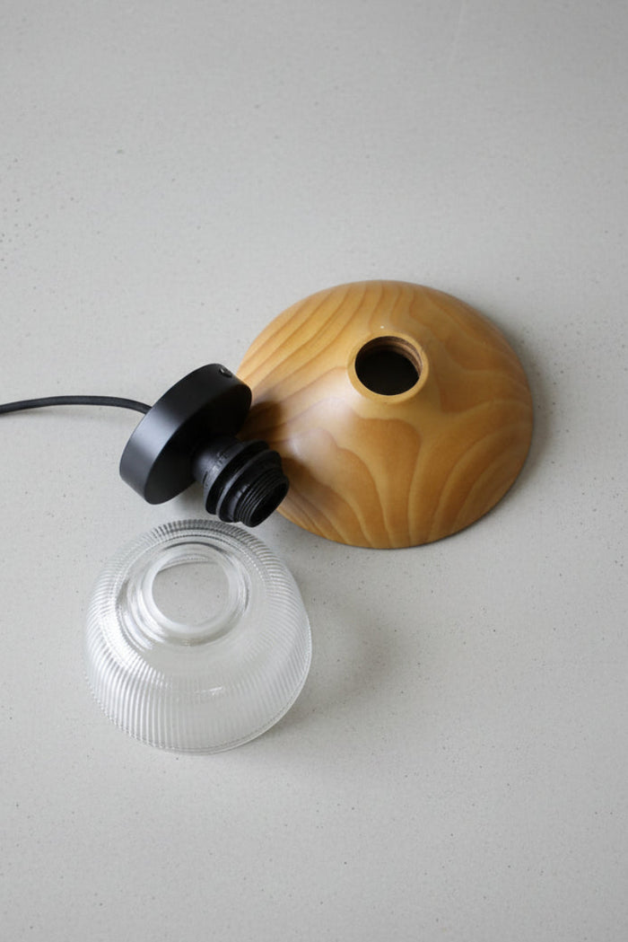 uninstalled product flat lay image showing the circular wood block, black batten holder and clear glass shade on a concrete surface.