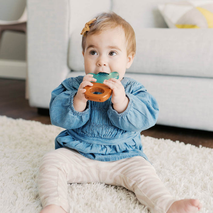Toddler sitting on a rug next to a couch while teething on an AquaCool Water-filled Teether