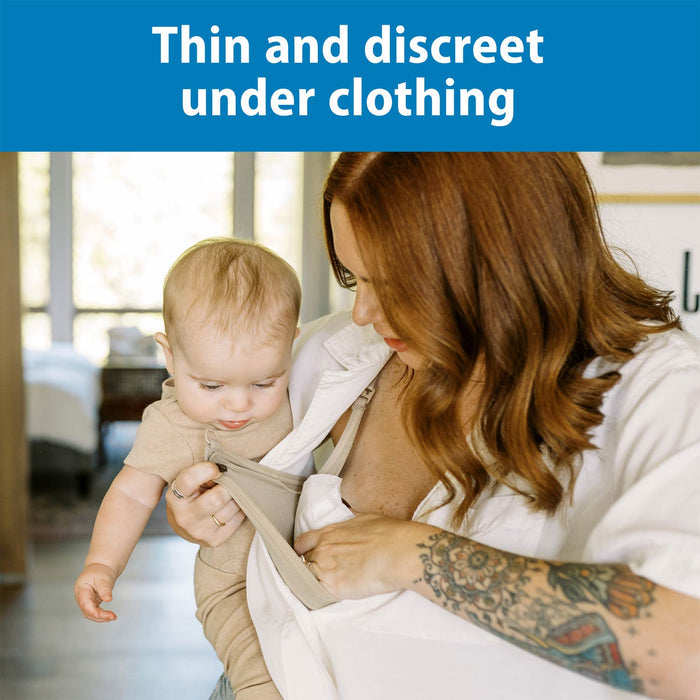 A tattooed woman holds a baby while adjusting Dr. Brown's™ Disposable Breast Pads under her shirt. Text above reads, "Thin and discreet under clothing with leak protection and a quick-absorbing core.
