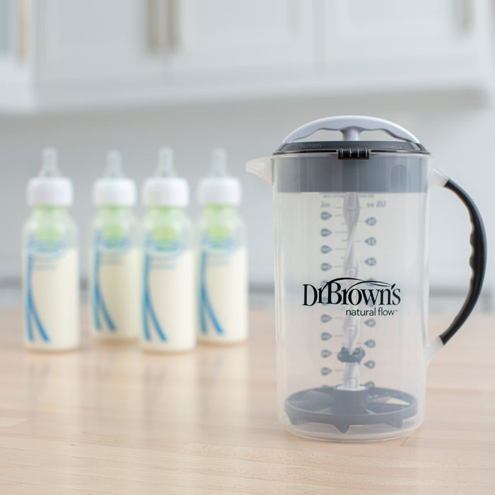 Dr. Brown's® Formula Mixing Pitcher from Dr. Brown's sits on a kitchen counter with four baby bottles behind it—ideal for prepping formula and designed to help reduce gas for your little one.