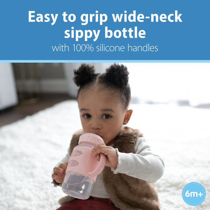 A toddler sits on a rug drinking from Dr. Brown's Milestones Wide-Neck Sippy Spout Bottle with Silicone Handles, 9 oz. Text highlights features like the silicone sippy spout, ideal for an easy transition from bottle to cup.