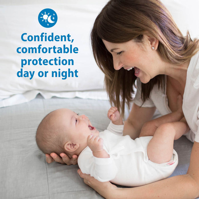 A smiling woman playfully holds a laughing baby on a bed. Blue text reads, "Confident, comfortable protection day or night," with sun and moon icons—perfect for those who trust Dr. Brown's™ Reusable Breast Pads by Dr. Brown's.