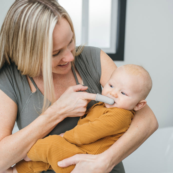 An adult uses Dr. Brown's Silicone Finger Toothbrush and Storage Case, 2-Pack to clean a baby's nose while gently holding the baby in their arms.