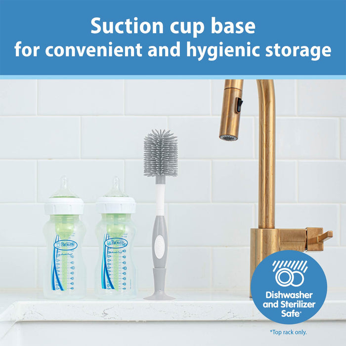 Bottle and brush set with suction cup base on a kitchen sink, featuring a gold faucet.