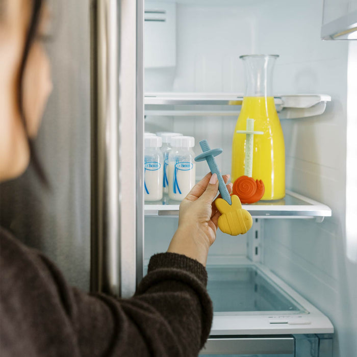 Person putting bee-shaped teething tube in fridge next to snail-shaped teething tube