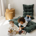 Two children sitting on green cushions reading a book in a cozy room.