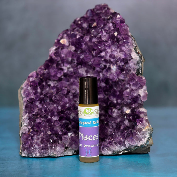 Pisces Aromatherapy Roll-on bottle in front of a large amethyst crystal on a blue surface.